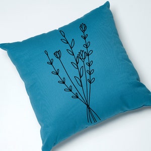 May include: A teal blue throw pillow with a black embroidered design of a bouquet of stylized flowers.