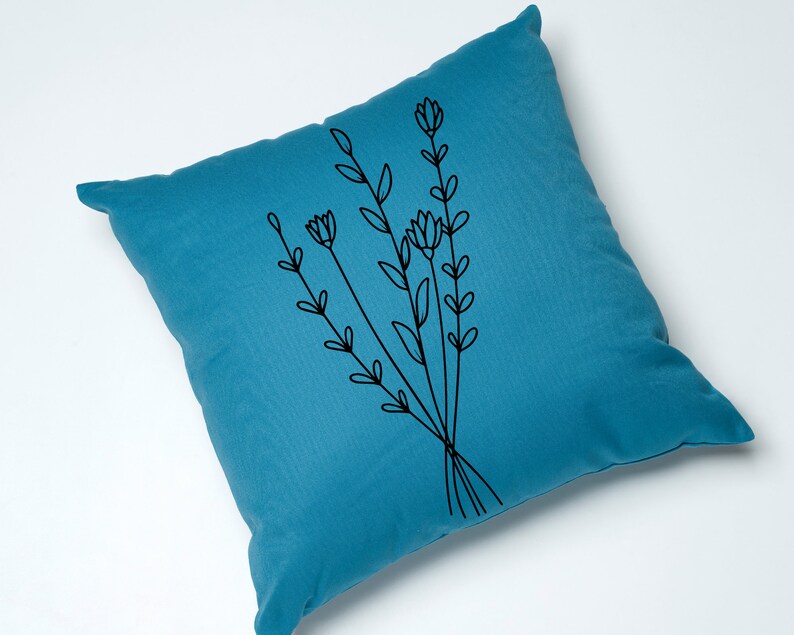 May include: A teal blue throw pillow with a black embroidered design of a bouquet of stylized flowers.