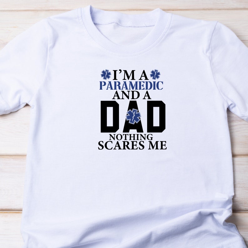 May include: White t-shirt with a black and blue graphic that says "I'm a Paramedic and a Dad. Nothing Scares Me."