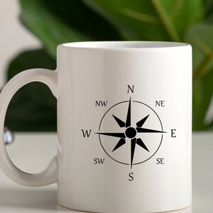May include: White ceramic mug with a black compass design. The compass has the directions N, NE, E, SE, S, SW, W, and NW.