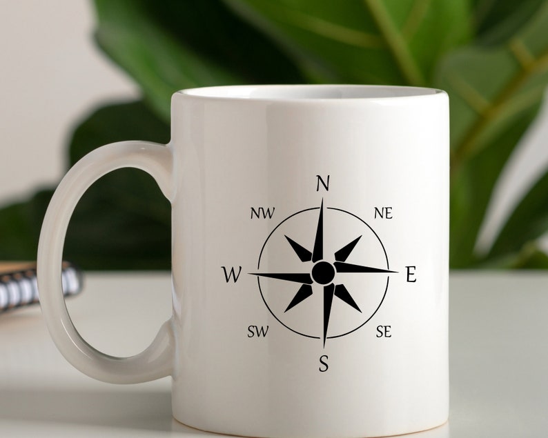May include: White ceramic mug with a black compass design. The compass has the directions N, NE, E, SE, S, SW, W, and NW.