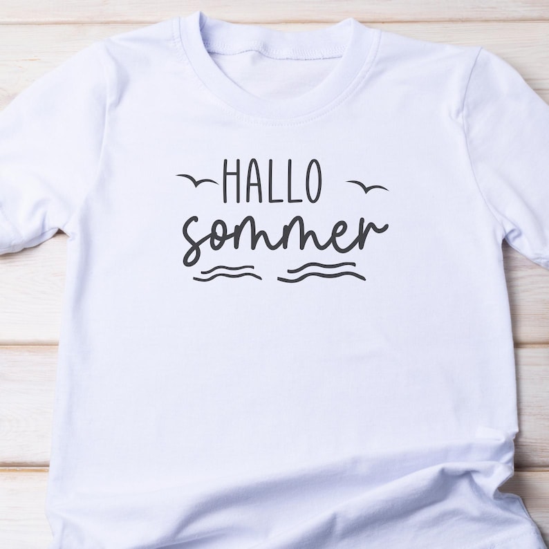 Puede incluir: Camiseta blanca con el texto "Hallo Sommer" en letras negras. El texto est&aacute; estilizado con una l&iacute;nea ondulada debajo y dos p&aacute;jaros volando arriba.