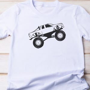 May include: A white t-shirt with a black silhouette of a monster truck on the front.