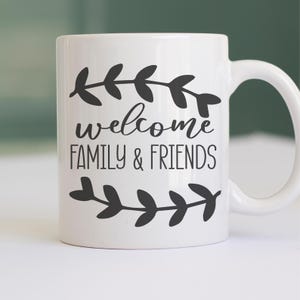 May include: White ceramic coffee mug with black text and leaf designs that reads "welcome family & friends".
