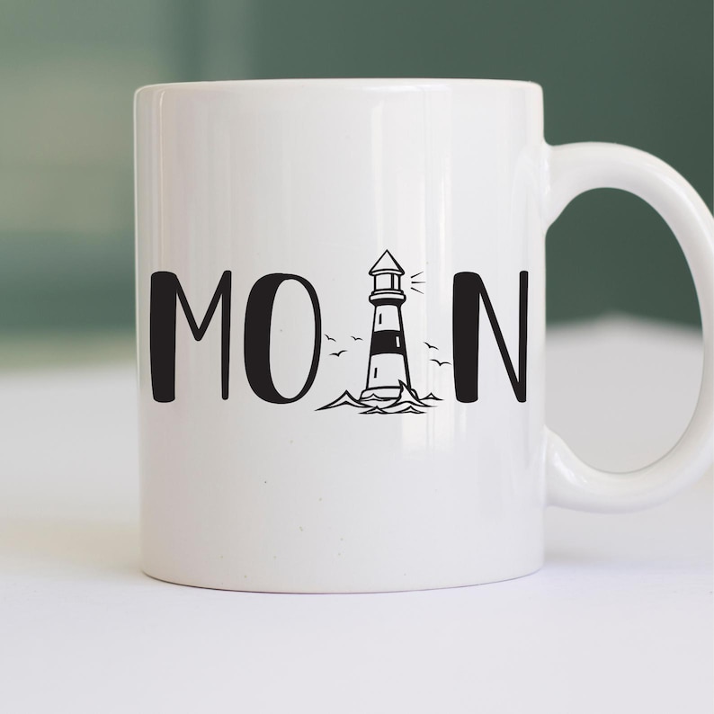 Puede incluir: Taza de cer&aacute;mica blanca con un gr&aacute;fico de faro negro y la palabra "MOAN" impresa en ella.