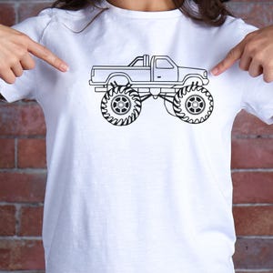 May include: A white t-shirt with a black line drawing of a monster truck. The truck has large tires and a pickup truck bed.