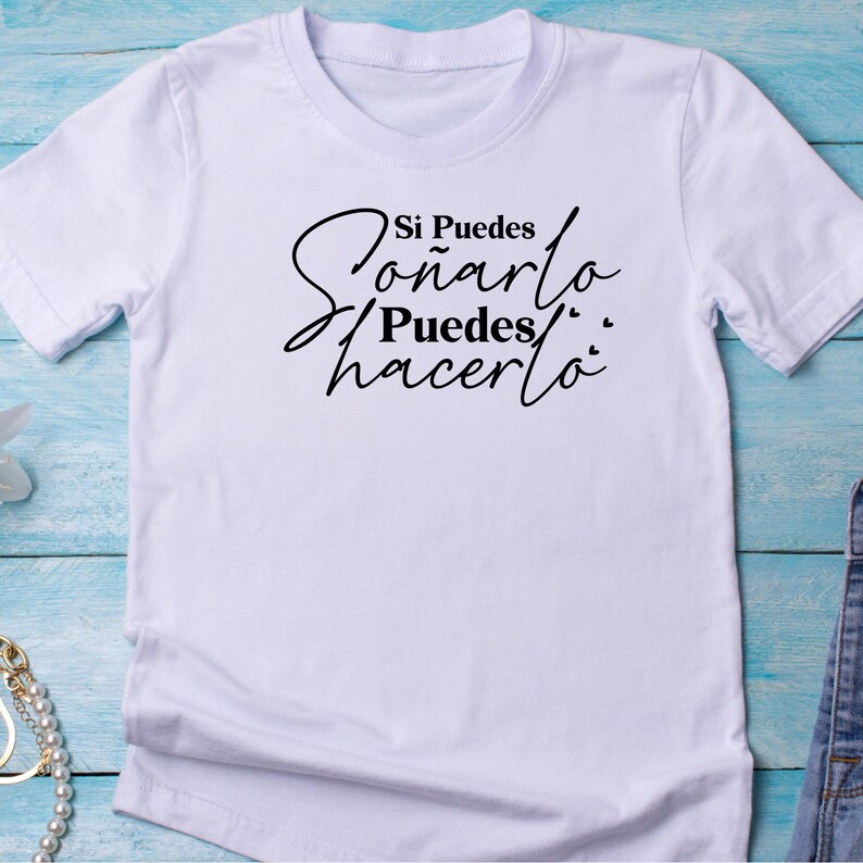 May include: White t-shirt with black text that reads "Si Puedes So&ntilde;arlo Puedes Hacerlo".