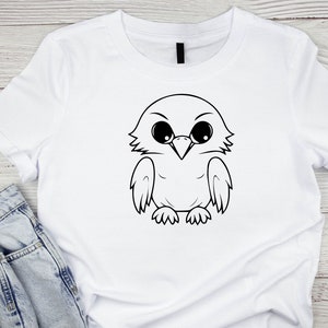 May include: White t-shirt with a black and white cartoon illustration of an owl with large eyes.