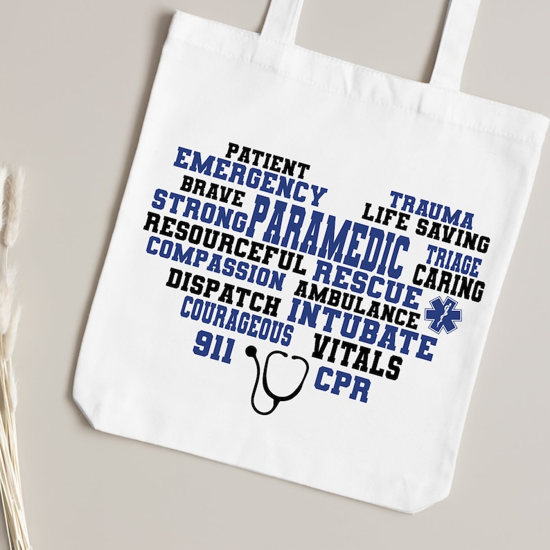 May include: White tote bag with a blue and black word cloud design that reads "Patient, Emergency, Brave, Strong Paramedic, Resourceful Rescue, Compassion, Ambulance, Dispatch, Intubate, Courageous, Vitals, 911, CPR". A stethoscope is below the word cloud.