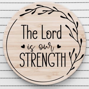 May include: A round wooden sign with a black floral design and the text "The Lord is our STRENGTH" in black lettering.