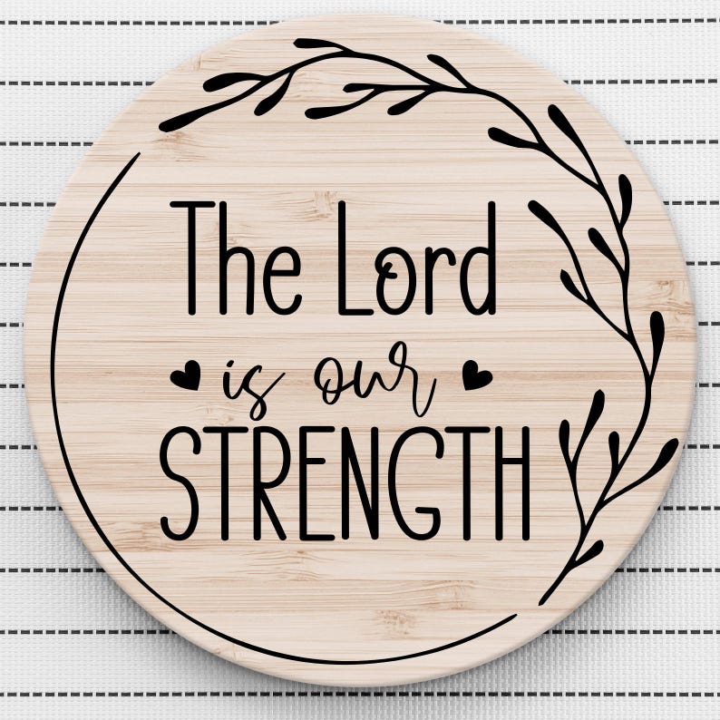 May include: A round wooden sign with a black floral design and the text "The Lord is our STRENGTH" in black lettering.