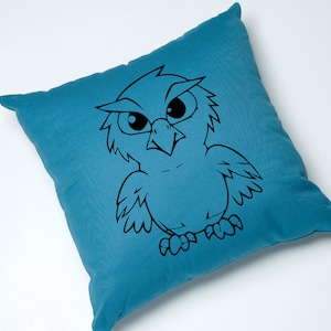 May include: A teal blue throw pillow with a black and white cartoon owl design. The owl has large eyes and a fierce expression.
