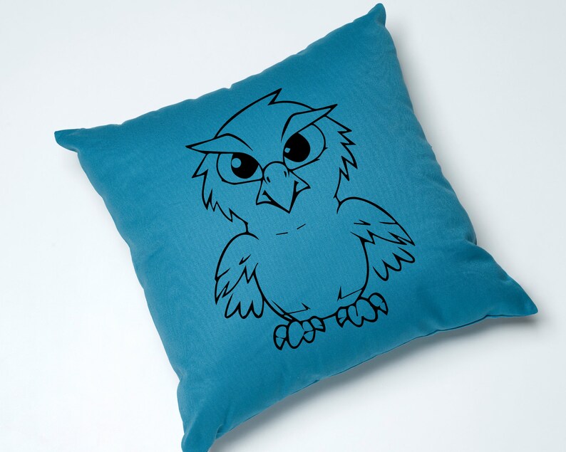 May include: A teal blue throw pillow with a black and white cartoon owl design. The owl has large eyes and a fierce expression.