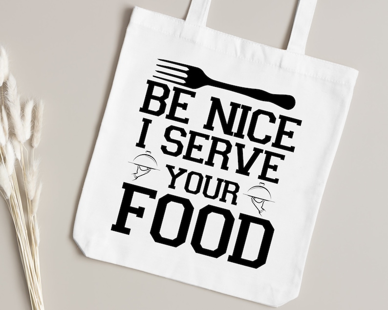May include: White tote bag with black text that reads "Be Nice I Serve Your Food". The text is in a bold, blocky font. A black fork and a black serving dish are also pictured on the bag.