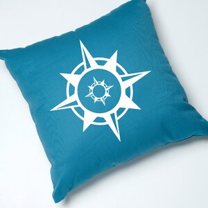 May include: A teal blue throw pillow with a white compass design. The compass has a circle with eight points.