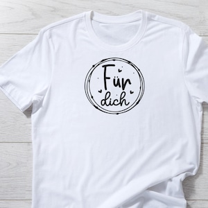 May include: White t-shirt with a crew neck. The shirt features a black circular design with the German text "F&uuml;r dich" inside. The design is surrounded by a dotted border.