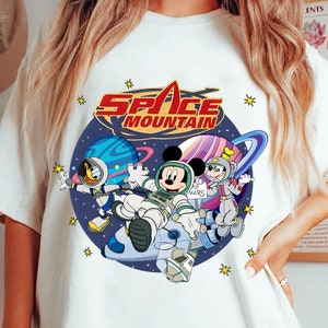 May include: White t-shirt with a colorful graphic of Mickey Mouse, Donald Duck, and Goofy dressed as astronauts. The graphic includes the text "Space Mountain".