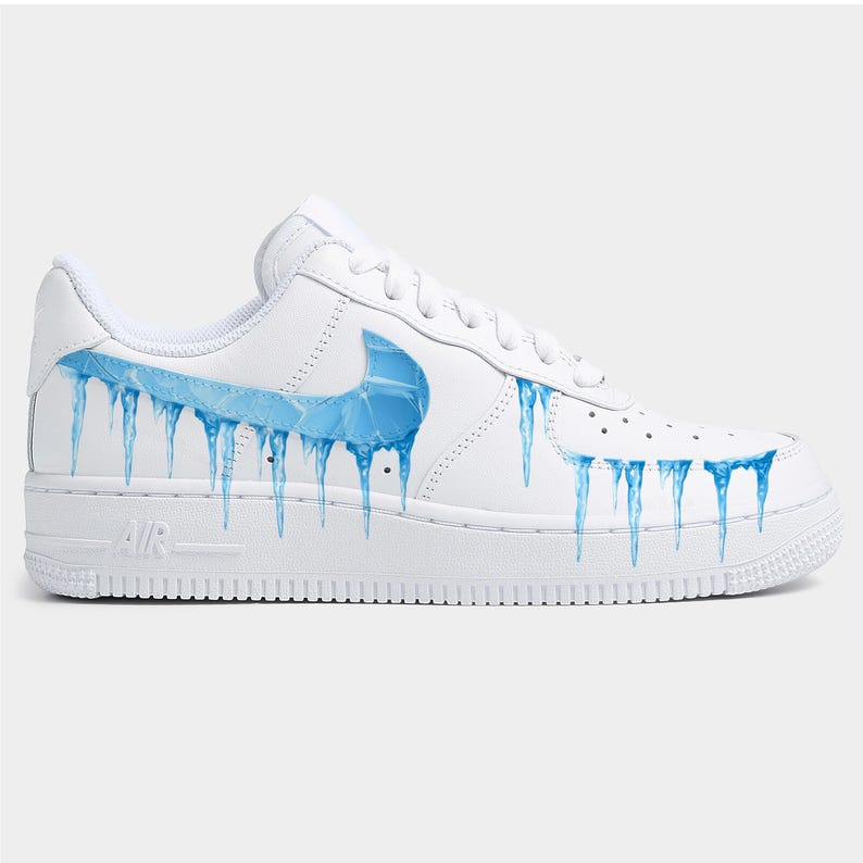 May include: White leather sneaker with a blue swoosh logo and blue icicle design. The shoe features a white sole and laces, with the word "AIR" printed on the side.