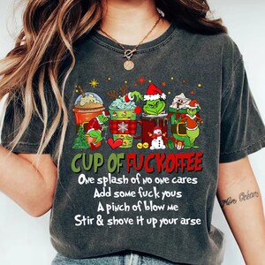Puede incluir: Camiseta gris oscuro con un gráfico humorístico de cuatro tazas de café de dibujos animados, cada una con un personaje de Grinch. El texto dice "CUP OF FUCKOFFEE" y una receta divertida.