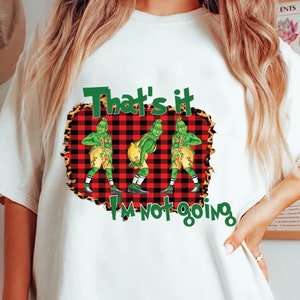 Puede incluir: Camiseta blanca con un gráfico del Grinch en varias poses, sobre un fondo a cuadros rojo y negro con un borde de estampado de leopardo. El texto "That's it I'm not going" se muestra en verde y blanco.