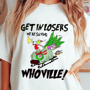 May include: White t-shirt with a graphic featuring the Grinch in a sleigh, a Christmas tree, and the text "GET IN LOSERS WE'RE SAVING WHOVILLE!". The Grinch is wearing a Santa hat and holding a yellow sign.