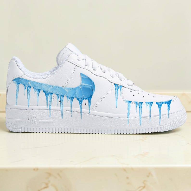 May include: White athletic shoe with a blue ice design. The shoe features a blue swoosh and blue icicles dripping down the side. The word "AIR" is visible on the sole.