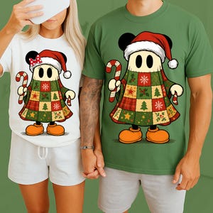 Puede incluir: Dos camisetas, una blanca y otra verde, cada una con un personaje de dibujos animados vestido con un atuendo navideño de patchwork. El personaje lleva un gorro de Papá Noel, sostiene un bastón de caramelo y tiene orejas negras y zapatos naranjas. El diseño es festivo.