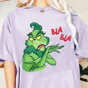 Puede incluir: Una camiseta lila con un personaje de dibujos animados verde, que muestra una expresión irritada y las palabras rojas "BLA BLA". El personaje gesticula con la mano, transmitiendo una actitud de rechazo.
