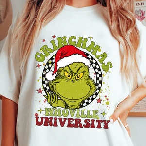 May include: A white t-shirt with a green Grinch wearing a red Santa hat. The Grinch is in a circle with the words "Grinchmas" and "Whoville University" below.