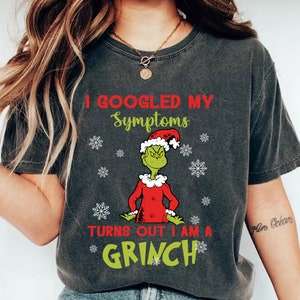 Könnte beinhalten: Dunkelgraues T-Shirt mit dem Text "I Googled My Symptoms Turns Out I Am A Grinch" in Rot und Grün. Das Shirt zeigt eine Cartoon-Figur des Grinch mit Weihnachtsmütze und Schneeflocken.