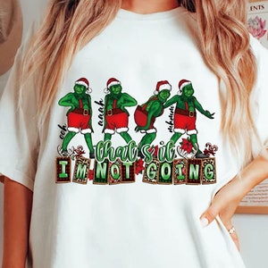 Puede incluir: Camiseta blanca con un diseño del Grinch verde con gorro de Papá Noel y pantalones cortos rojos, con el texto "that's it I'm not going". El Grinch está en varias poses. El diseño incluye bastones de caramelo y poinsettias.
