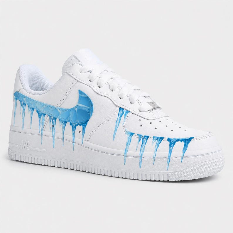 May include: White leather sneaker with a blue ice design. The shoe features a blue Nike swoosh and blue icicles dripping down the side. The sole is white with the word "AIR" in white.