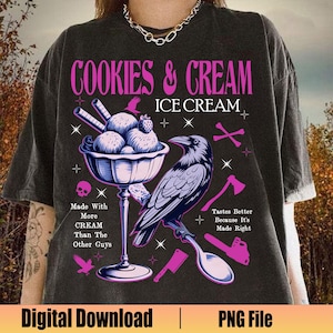 May include: A black t-shirt with a pink graphic design featuring a cartoon ice cream cone with a raven perched on the side. The text "Cookies & Cream Ice Cream" is written in pink letters above the ice cream cone. The text "Made With More Cream Than The Other Guys" is written in white letters on the left side of the ice cream cone. The text "Tastes Better Because It's Made Right" is written in white letters on the right side of the ice cream cone.