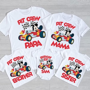 May include: A set of five white t-shirts featuring a cartoon image of Mickey Mouse driving a race car. The shirts have the text "Pit Crew" and different family member titles: "Papa", "Mama", "Brother", "Sister", and "Birthday Boy Sam".