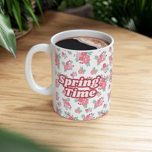 May include: White ceramic mug with a floral pattern and the text "Spring Time" in red. The mug is filled with coffee.