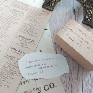 May include: A wooden stamp with the text "Time goes by so fast - People go in and out of my life. Again 19" engraved on it. The stamp is sitting on a piece of paper with the same text printed on it.