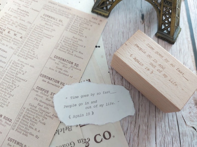 May include: A wooden stamp with the text "Time goes by so fast - People go in and out of my life. Again 19" engraved on it. The stamp is sitting on a piece of paper with the same text printed on it.