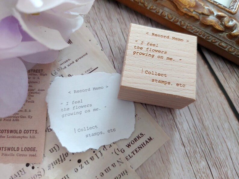 May include: A wooden stamp with the text "< Record Memo >" "I feel the flowers growing on me." | Collect stamps, etc" on it. The stamp is sitting on a piece of paper with the same text.