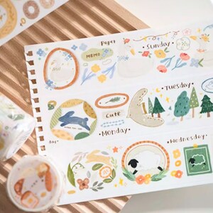 May include: A set of decorative washi tapes featuring various designs, including a cute bunny, a sheep, and a forest scene. The tapes are printed on a white background with colorful illustrations. The text on the tapes includes "Sunday", "Tuesday", "Wednesday", "Monday", "Cute", "Paper Memo", and "To".