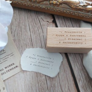 May include: A wooden stamp with the text "*(Trouvaille) / Hygge & Sobremesa --| Ethereal | & Serendipity:"  The stamp is sitting on a wooden surface.