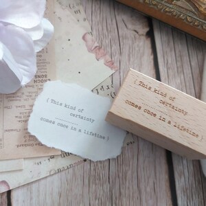 May include: A wooden stamp with the text "(This kind of certainty comes once in a lifetime)" on it. The stamp is light brown and has a rectangular shape.