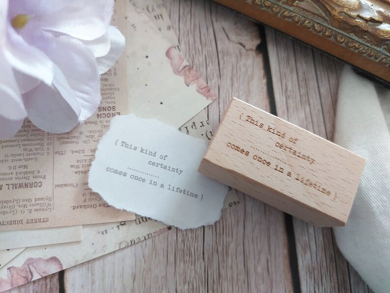 May include: A wooden stamp with the text "(This kind of certainty comes once in a lifetime)" on it. The stamp is light brown and has a rectangular shape.