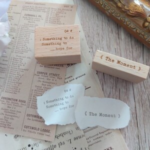 May include: Two wooden stamps with text. The first stamp is light brown and reads "04 # : Something to do Something to - hope for". The second stamp is a darker brown and reads "<The Moment>".