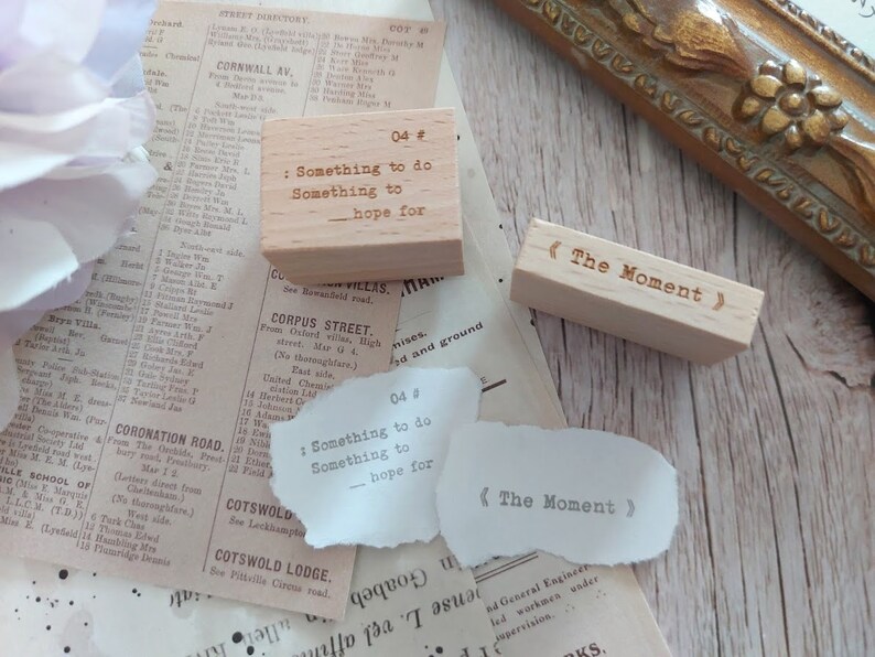 May include: Two wooden stamps with text. The first stamp is light brown and reads "04 # : Something to do Something to - hope for". The second stamp is a darker brown and reads "<The Moment>".