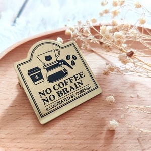 May include: Gold metal sign with a black and white illustration of a coffee pot and a coffee cup. The sign reads "No Coffee No Brain" and "Illustrated by Cubefish".