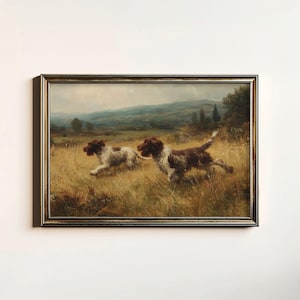 May include: Framed vintage painting of two dogs running through a field. The dogs have brown and white fur. The painting has a gold-colored frame and depicts a landscape with hills and trees in the background.