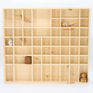 May include: A wooden display shelf with many small compartments. The shelf contains a small ceramic vase, a wooden block, a figurine, and a teddy bear. The shelf is made of light-coloured wood and is designed for displaying small collectibles.