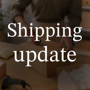 May include: A brown cardboard shipping box being prepared for transit. The text Shipping update is overlaid in large white serif font across the center of the image. A black barcode scanner is visible in the lower left corner of the workspace.