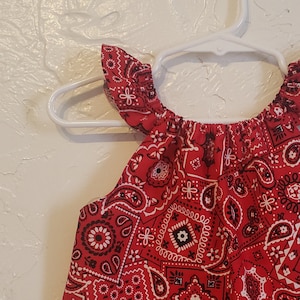 May include: A red sleeveless top with a bandana print. The top has ruffles on the shoulders.