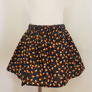 Może przedstawiać: Czarna spódnica z nadrukiem w kształcie cukierków kukurydzianych. Spódnica ma elastyczną gumkę w pasie i jest wykonana z miękkiej, wygodnej tkaniny.